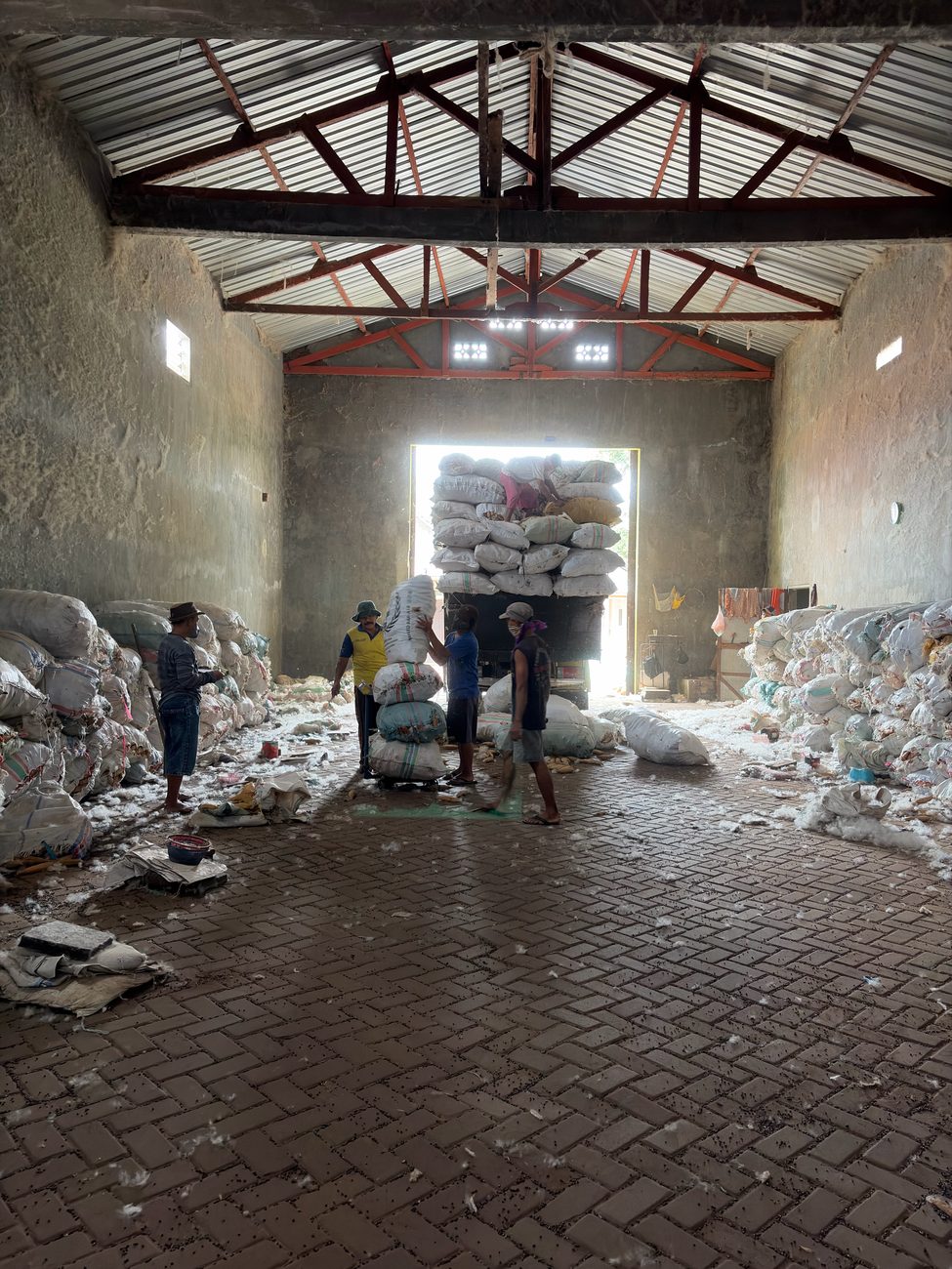 Inside our East Java gudang — workers, stacked sacks, and loose kapok floss