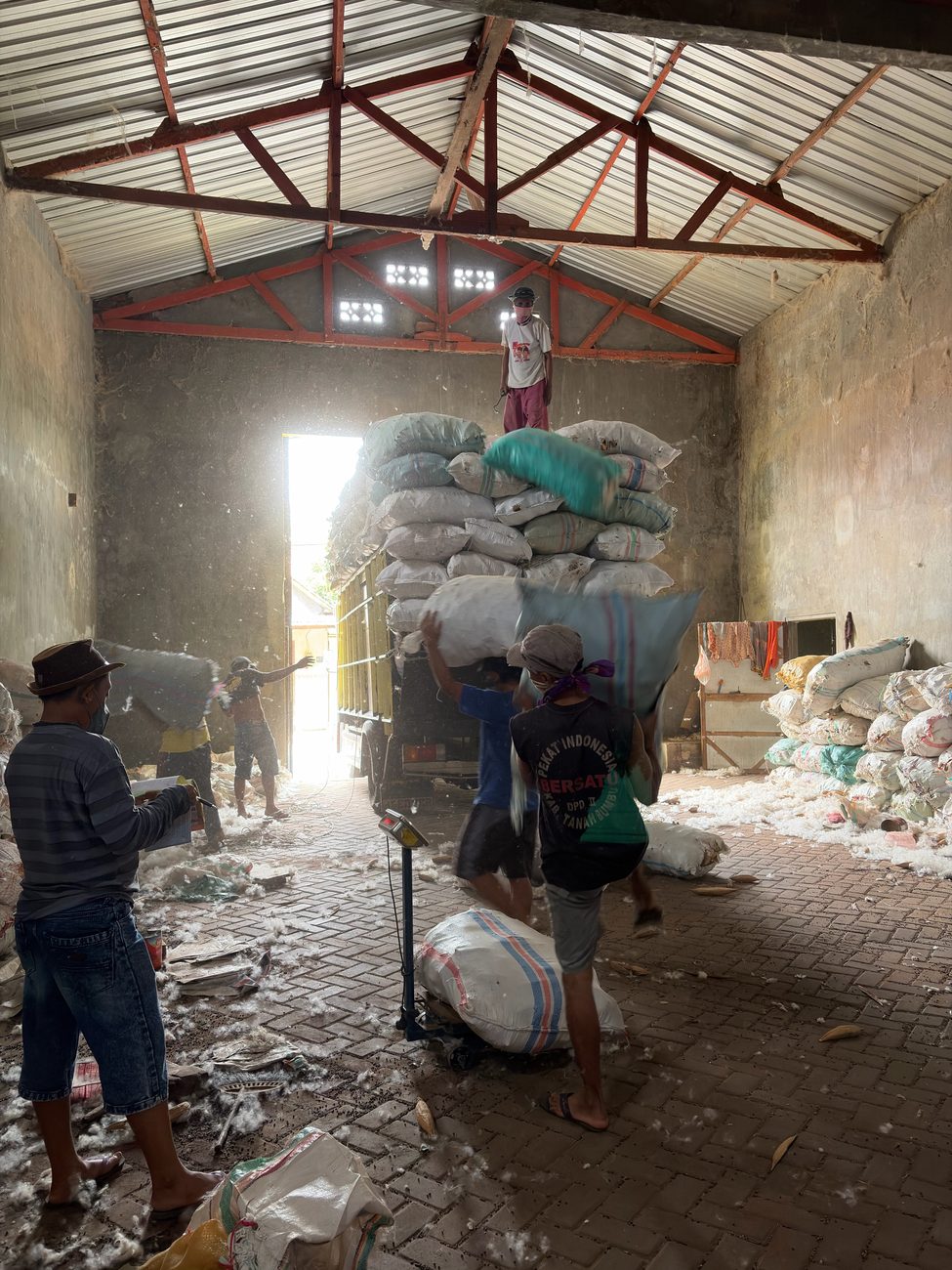Workers loading sacks of kapok onto a truck inside the gudang